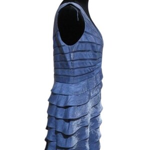 May include: A sleeveless, blue dress with a V-neck and layered, ruffled skirt. The dress has a textured appearance and is displayed on a black mannequin. The dress is a solid color and appears to be made of a lightweight fabric.