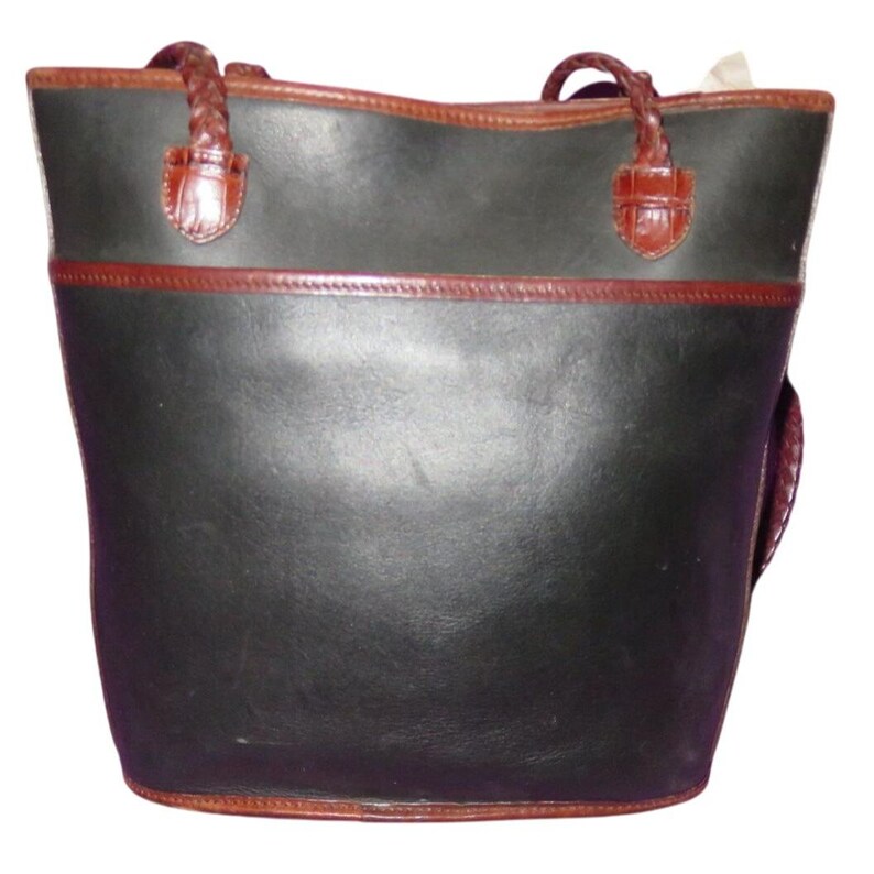 May include: Black leather tote bag with brown trim and braided handles. The bag features a structured design with a rectangular base and a wider top opening. The handles are attached with decorative brown leather accents.