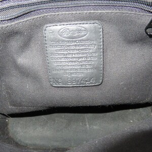 May include: Black leather handbag interior with a stitched leather tag. The tag features the Brighton logo and text that reads "The Brighton Collection handbags are individually crafted from quality leathers." The tag also has the number 897414.