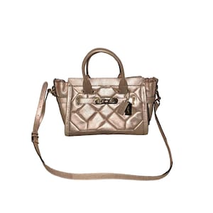 May include: A metallic rose-gold handbag with a quilted diamond pattern. The bag has a top handle and a detachable shoulder strap. It features a clasp closure and a small tag. The bag is made of a shiny, textured material.