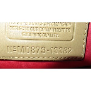 Op de afbeelding: Close-up van een beige lederen label met de tekst "This superior craftsmanship reflects our commitment to enduring quality." en het nummer "N&deg;M0873-13382".