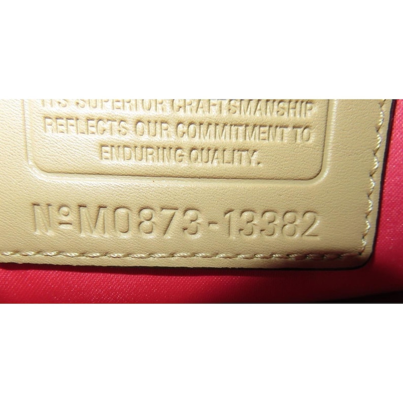 Op de afbeelding: Close-up van een beige lederen label met de tekst "This superior craftsmanship reflects our commitment to enduring quality." en het nummer "N&deg;M0873-13382".