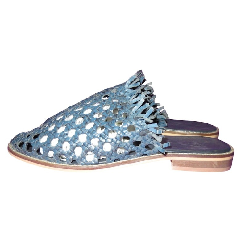 May include: Blue woven leather slip-on sandals with a flat sole. The open-weave design allows for breathability, and the fringe detail adds a stylish touch. These sandals are perfect for casual wear.