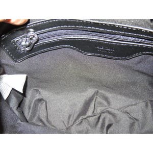 May include: Black handbag interior with a silver zipper and a decorative zipper pull. The interior is lined with black fabric. The brand name "Valentino" is visible on the leather trim. A white tag is visible on the left side.