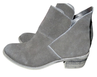 May include: A pair of black suede ankle boots. The boots have a low heel and a unique cut-out design on the sides. The boots are made of a soft, matte material and appear to be unworn.