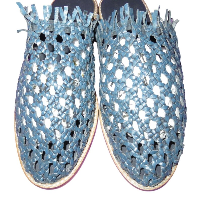 May include: A pair of blue woven leather slip-on shoes. The shoes have an open weave design, allowing glimpses of the white interior. The edges are trimmed with a light-colored material, and the top edge has a fringe detail.