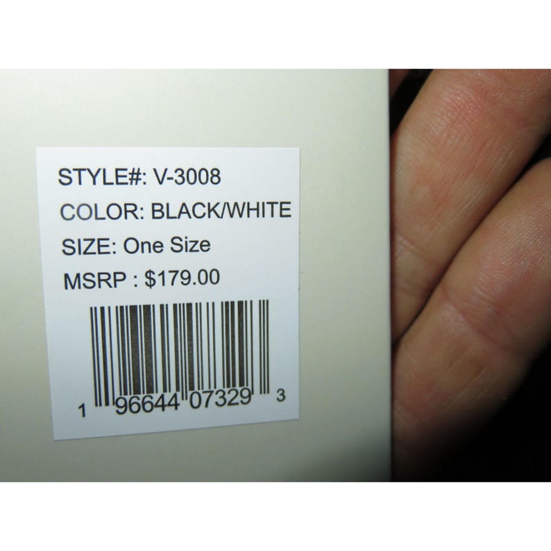 May include: A white product tag with the text "STYLE#: V-3008", "COLOR: BLACK/WHITE", and "SIZE: One Size". A barcode and the number "1" are at the bottom. The tag is held by a person.
