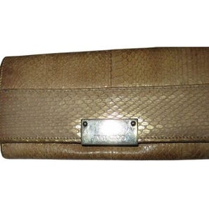 Op de afbeelding: Een bruinleren clutch met een slangenpatroon. De clutch heeft een rechthoekige zilverkleurige metalen plaat met de merknaam "JIMMY CHOO" erop. De clutch is gesloten.