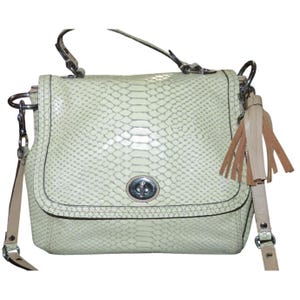 May include: A cream-colored handbag with a snakeskin pattern. The bag features a flap closure with a silver-tone clasp, a top handle, and a detachable shoulder strap. A leather tassel hangs from the side. The bag's dimensions are not visible.