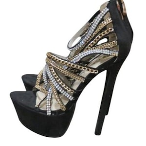 May include: Black platform high heels with gold and silver chain and rhinestone accents. The open-toe sandals have a stiletto heel and a zipper closure on the back. The shoes have a platform sole.
