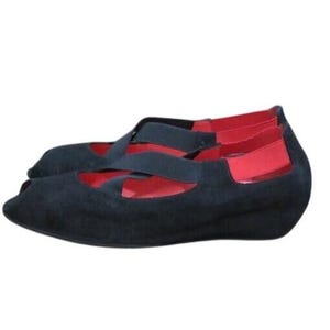 Pode incluir: Um par de sapatos pretos peep-toe com interior e detalhes vermelhos. Os sapatos têm um salto cunha baixo e tiras cruzadas na parte superior do pé. Os sapatos são feitos de um material macio, semelhante a camurça.