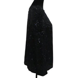 Op de afbeelding: Een zwarte top met pailletten op een mannequin. De top is bedekt met kleine, reflecterende pailletten, waardoor een glinsterend effect ontstaat. Het kledingstuk heeft een ronde halslijn en een iets losse pasvorm, geschikt voor avondkleding of speciale gelegenheden.