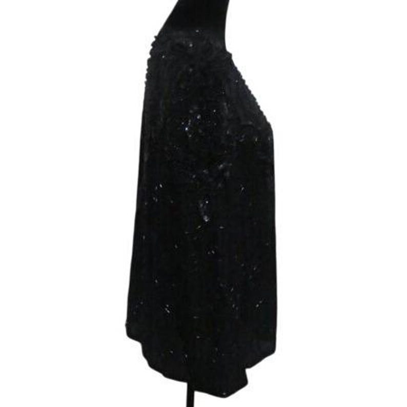 Op de afbeelding: Een zwarte top met pailletten op een mannequin. De top is bedekt met kleine, reflecterende pailletten, waardoor een glinsterend effect ontstaat. Het kledingstuk heeft een ronde halslijn en een iets losse pasvorm, geschikt voor avondkleding of speciale gelegenheden.