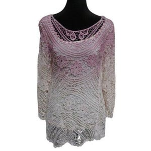 May include: A crochet top in a gradient of white to light pink, displayed on a black mannequin. The top features a scoop neckline and long sleeves. The crochet design includes floral and geometric patterns.