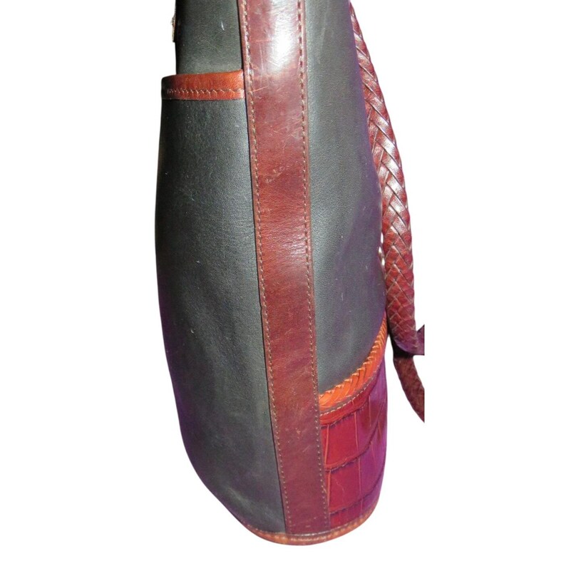 May include: A shoulder bag with a dark gray body, accented with brown leather trim and a braided strap. The bottom section features a red, textured, crocodile-like pattern.