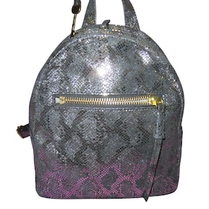 May include: A silver and black backpack with a snakeskin pattern and a gold zipper. The bottom of the backpack fades to a pink snakeskin pattern. The backpack has two small handles and a small gold key charm.