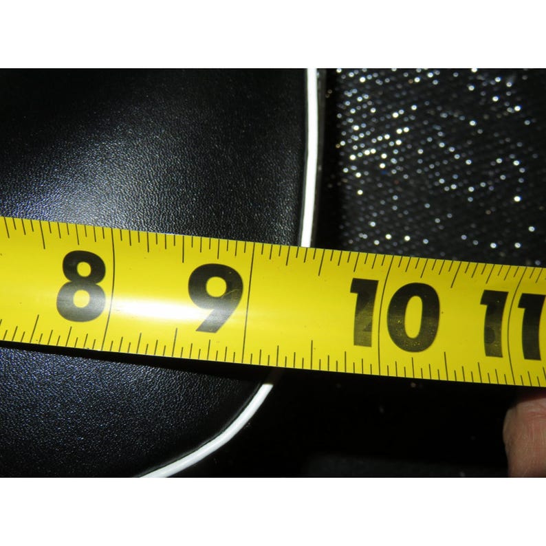 May include: A yellow measuring tape showing measurements in inches. The tape is positioned over a black surface with a white border. The tape reads from 8 to 11 inches.