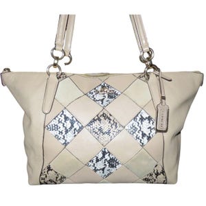 May include: Cream-colored leather tote bag with a diamond pattern. The bag features a patchwork design with cream, off-white, and snakeskin-print squares. It has two handles, silver hardware, and a Coach hang tag.