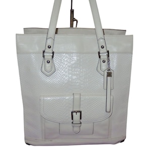 Könnte beinhalten: Cremefarbene Tragetasche mit einem strukturierten, schlangenlederartigen Muster auf der Vorder- und den Seiten. Die Tasche hat eine Vordertasche mit Schnallenverschluss, zwei Tragegriffe und silberfarbene Hardware.