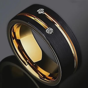 May include: A black ring with a gold interior and two gold bands with small, round, clear stones. The ring has a brushed metal texture on the exterior.