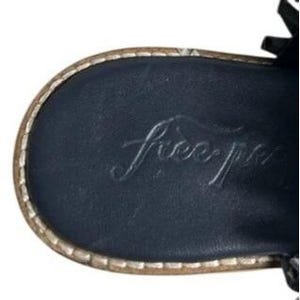 May include: Close-up of the sole of a black sandal with the embossed text "free people". The sole has a stitched, light brown border.
