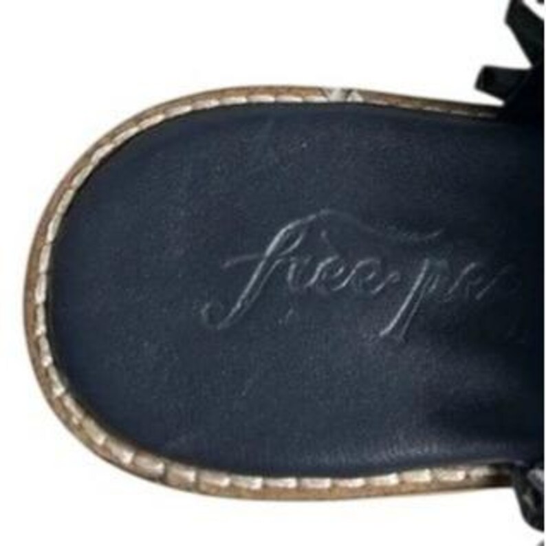 May include: Close-up of the sole of a black sandal with the embossed text "free people". The sole has a stitched, light brown border.