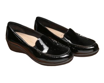 May include: A pair of black patent leather loafers with a low wedge heel. The shoes have a classic slip-on design with a rounded toe and a stitched vamp. The soles are a dark brown color.