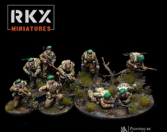 May include: A group of nine painted miniature figures of soldiers wearing green berets and carrying weapons. The figures are posed in a variety of combat stances and are set against a black background. The figures are painted in realistic detail, with visible details such as their uniforms, weapons, and facial features. The figures are all standing on small, circular bases.