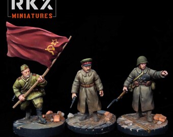 Può includere: Tre statuette di soldati in miniatura dipinte a mano su basi circolari. La figura a sinistra regge una grande bandiera rossa con un emblema giallo di martello e falce. La figura centrale indossa un lungo cappotto color marrone chiaro e un berretto.