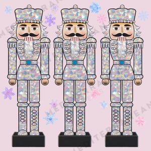 Może przedstawiać: Trzy srebrne, tęczowe figurki  łamacza orzechów z białymi brodami i niebieskimi akcentami. Łamacze orzechów stoją na czarnych podstawach na różowym tle.