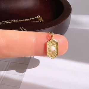 May include: A gold necklace with a pendant featuring a sunburst design and a white opal stone.