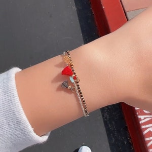May include: A bracelet with black beads and a silver chain with three charms. The charms are a red tassel, a blue tassel, and a gold coin.