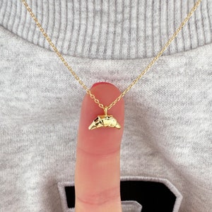 May include: A gold chain necklace with a small, gold croissant pendant.
