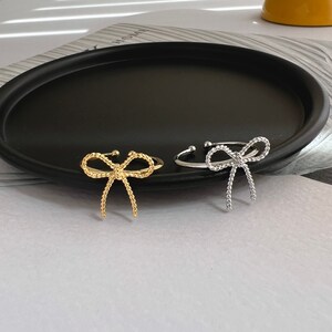 May include: Two adjustable rings with a bow design. One ring is gold and the other is silver.