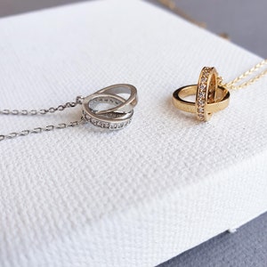 May include: Two delicate necklaces with a silver and gold pendant featuring a circle design with small clear stones. The necklaces are displayed on a white surface.