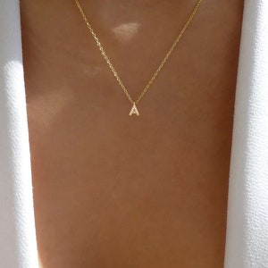 May include: A gold chain necklace with a small pendant in the shape of the letter A. The pendant is encrusted with tiny clear stones.