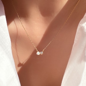 May include: A delicate gold chain necklace with a small opal and a clear gemstone pendant.