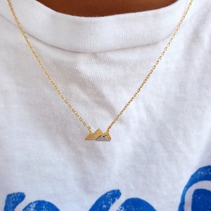 May include: A gold chain necklace with a small mountain pendant. The pendant is made of two metals, gold and silver.