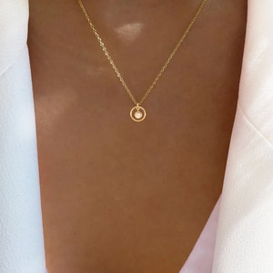 May include: A gold chain necklace with a small circle pendant featuring a white opal stone.
