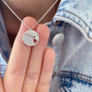 May include: A silver necklace with a circular pendant featuring an outline of the Hawaiian islands.