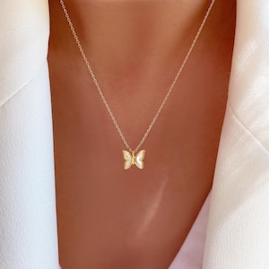 May include: A gold chain necklace with a delicate butterfly pendant. The butterfly is made of white enamel and has gold accents.