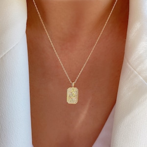 May include: A gold chain necklace with a rectangular pendant featuring a sun design with small clear stones.