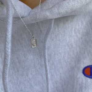 May include: A silver chain necklace with a small rectangular pendant featuring a crescent moon design.