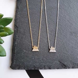 May include: Two delicate necklaces with a mountain pendant design. The pendants are made of silver and gold and are adorned with small, sparkling stones.