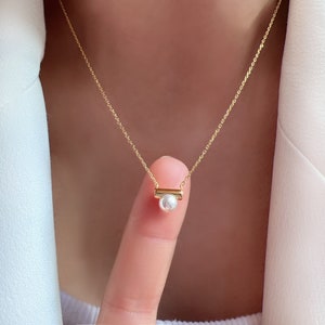 May include: A gold chain necklace with a small pearl and a gold bar pendant.