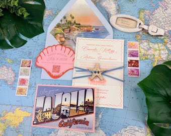 Può includere: Un set di partecipazioni di nozze con una cartolina di La Jolla California, un biglietto di risposta a forma di conchiglia con QR code e un invito principale fissato con spago blu e una stella marina, su uno sfondo di mappa del mondo.