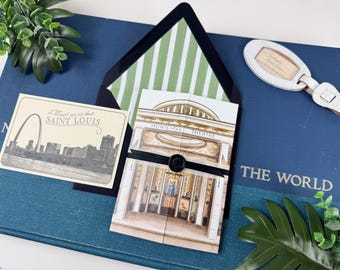 Può includere: Un set di cancelleria con una carta illustrata con lo skyline di Saint Louis e il testo Meet us in SAINT LOUIS, una carta piegata raffigurante il Municipal Theatre, fissata con un nastro nero e un sigillo, e un'etichetta per bagagli bianca.
