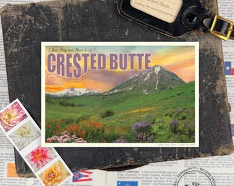 Può includere: Una cartolina rettangolare con un'illustrazione paesaggistica di Crested Butte con montagne innevate, colline verdi e fiori selvatici sotto un cielo al tramonto. Il testo recita Join Amy and Max in CRESTED BUTTE e SAVE THE DATE JUNE 19, 2021.