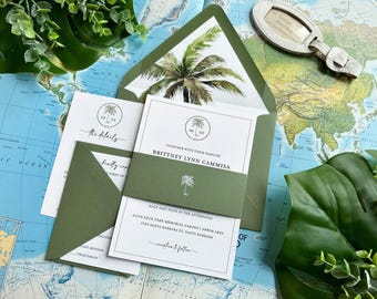 May include: A wedding invitation suite featuring white cards with black text and palm tree illustrations, held together by a solid olive green paper band. The set includes an olive green envelope with a palm tree print on the inner flap.