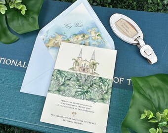 Puede incluir: Un conjunto de invitaciones con el tema de Key West. La tarjeta de invitación tiene una ilustración en acuarela de una iglesia y follaje tropical. El sobre tiene un mapa de Key West. También se incluye una etiqueta de equipaje blanca.